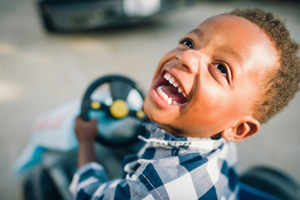 A young child laughing while sitting in a toy car