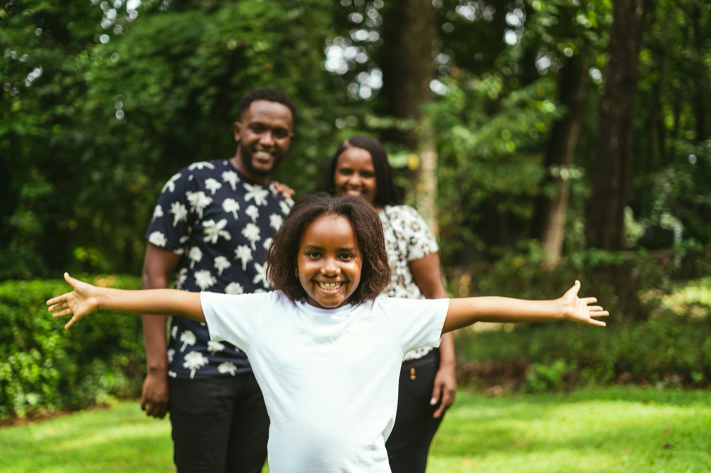 A family standing together on grass, the child's arms held wide